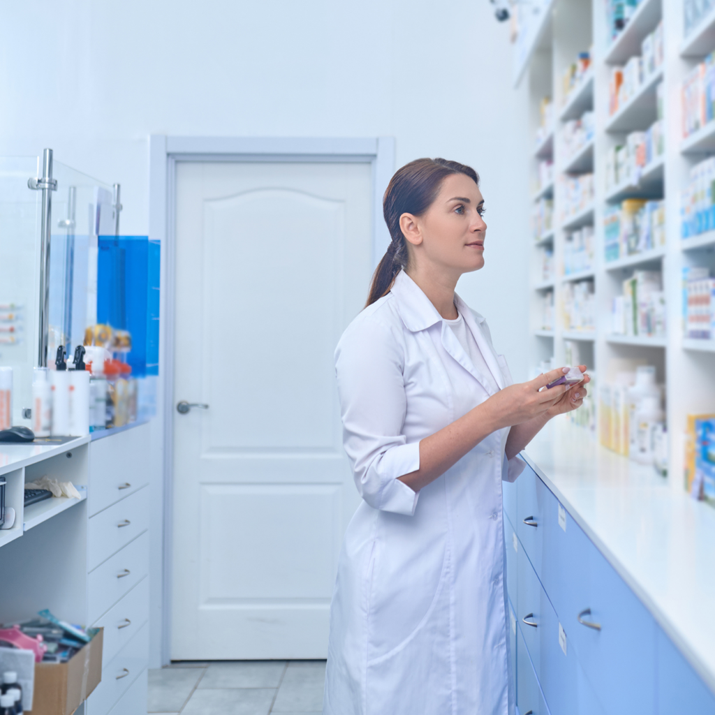 Eine Apothekenangestellte steht im Labor mit einem Medikament in der Hand vor einem Regal