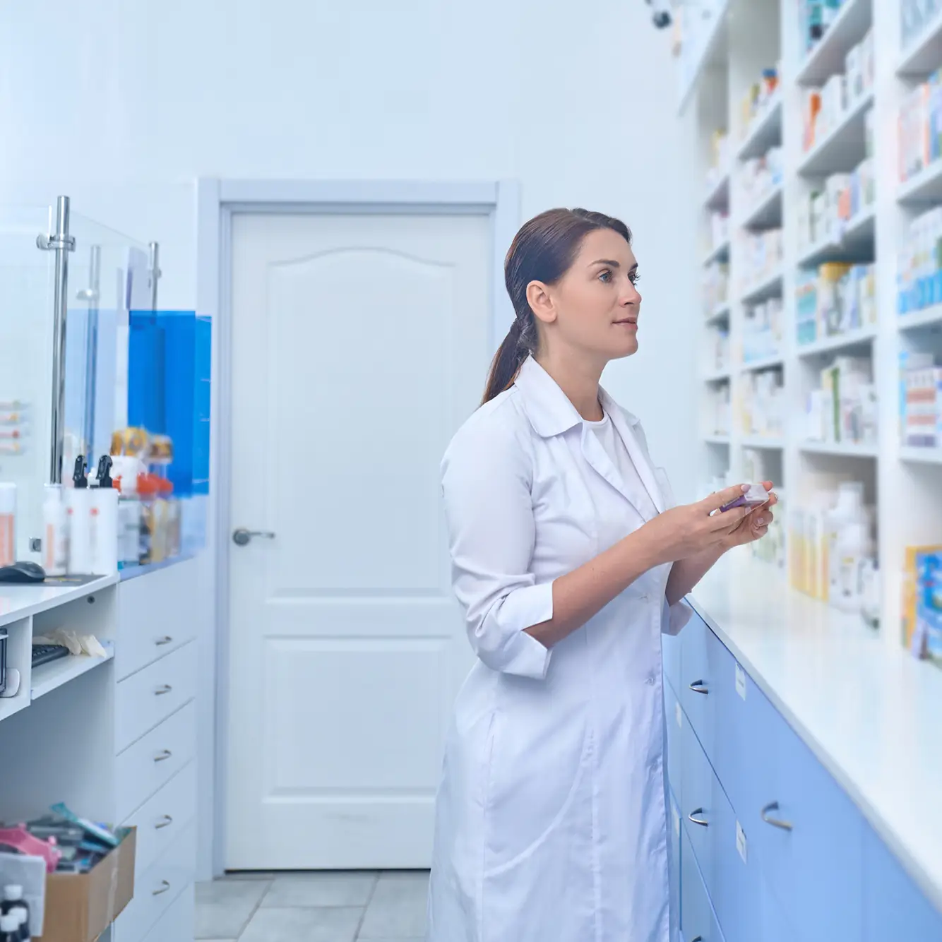 Eine Apothekenangestellte steht im Labor mit einem Medikament in der Hand vor einem Regal